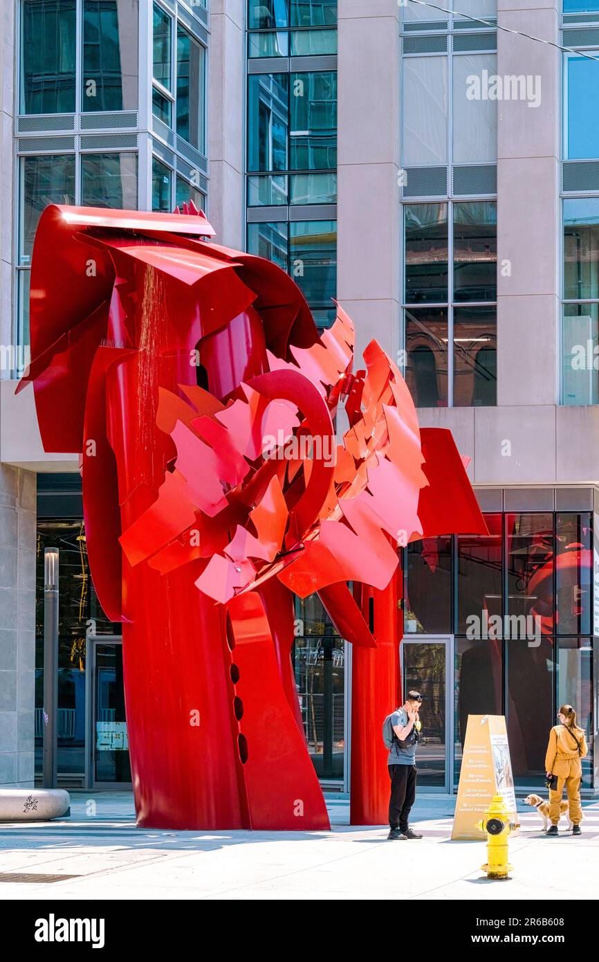 Toronto, Canada - June 4, 2023: People by a tall red metal sculpture in Yonge Street. The piece of art stands in front of a building. Stock Photo