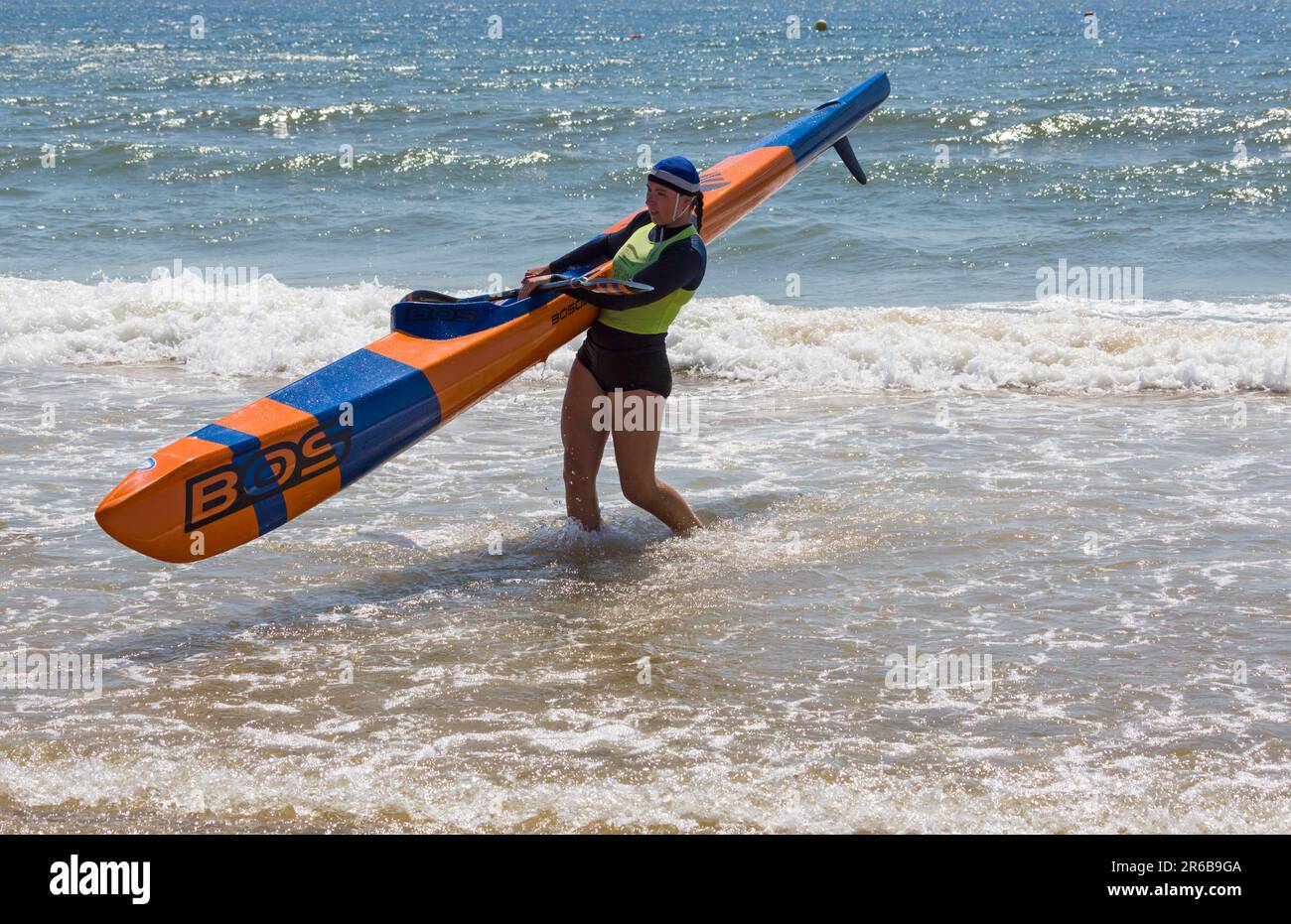 Young woman carrying a surf ski surfski, the Surf Life Saving GB GBR Beach Trial Weekend in the sea at Branksome Chine, Poole, Dorset, England UK in Stock Photo
