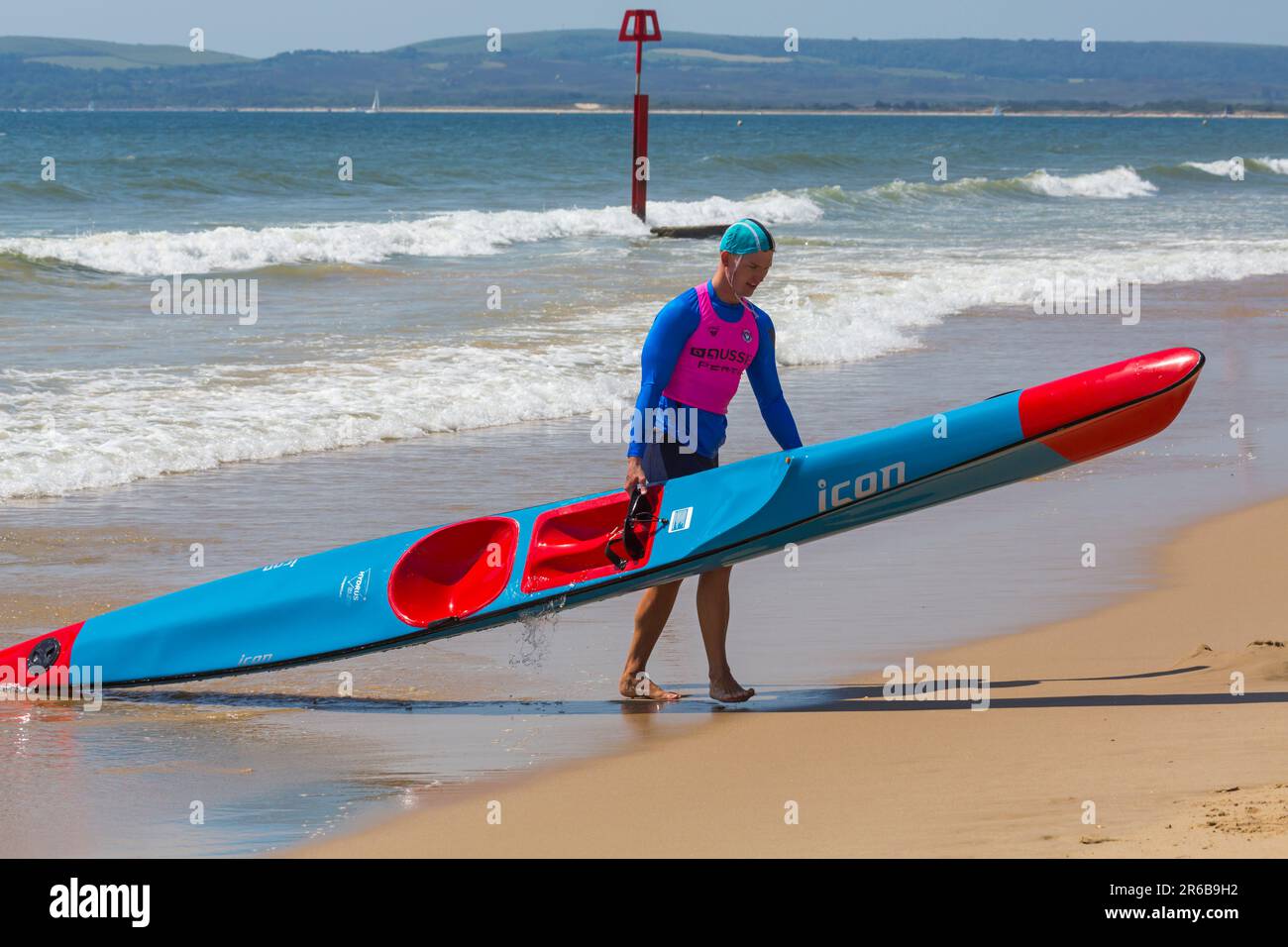 Young man carrying a surf ski surfski, the Surf Life Saving GB GBR Beach Trial Weekend at Branksome Chine, Poole, Dorset, England UK in June Stock Photo
