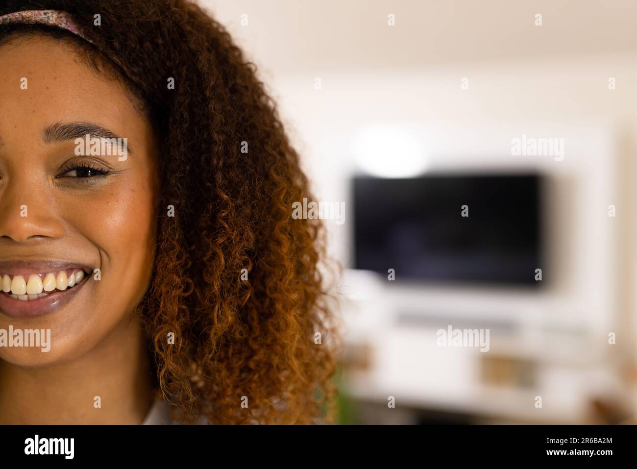 Half portrait of happy biracial woman with curly hair smiling to camera at home, copy space Stock Photo