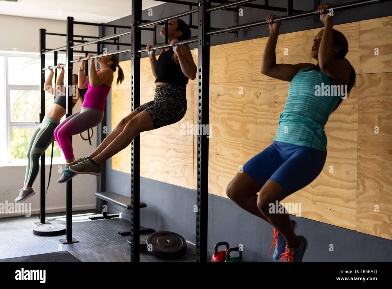 Multiracial females practicing chin-ups on gymnastic bars in health club Stock Photo