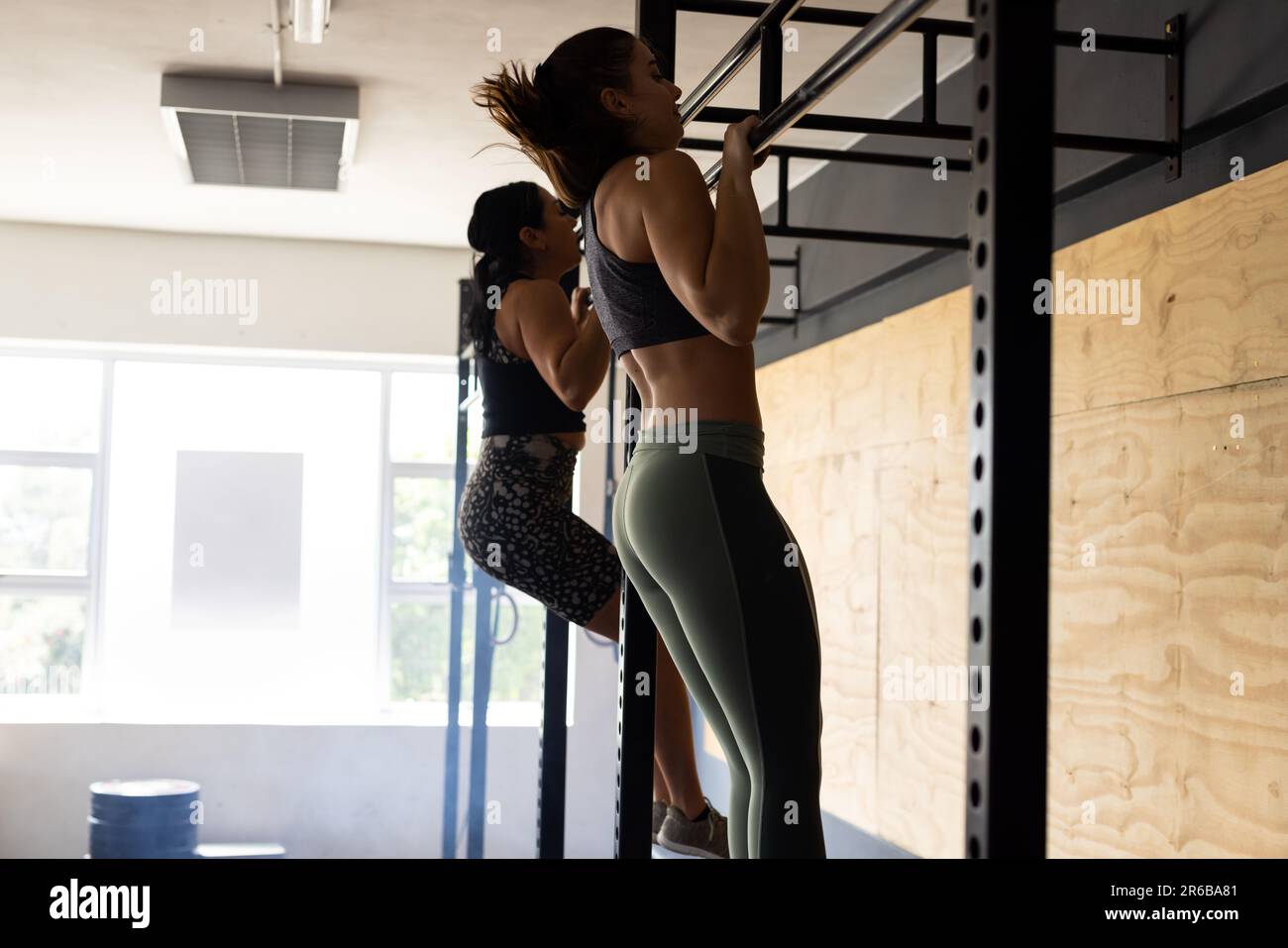 Side view of caucasian young women practicing chin-ups on gymnastics bar in health club, copy space Stock Photo