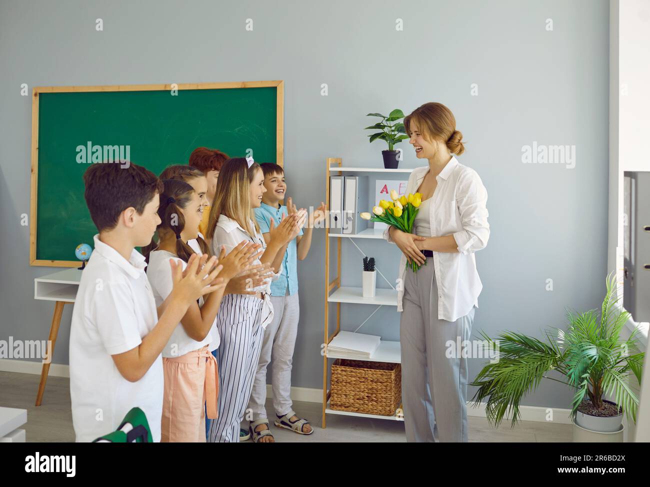 Children students giving flowers to their teacher clapping hands congratulating on holiday. Stock Photo