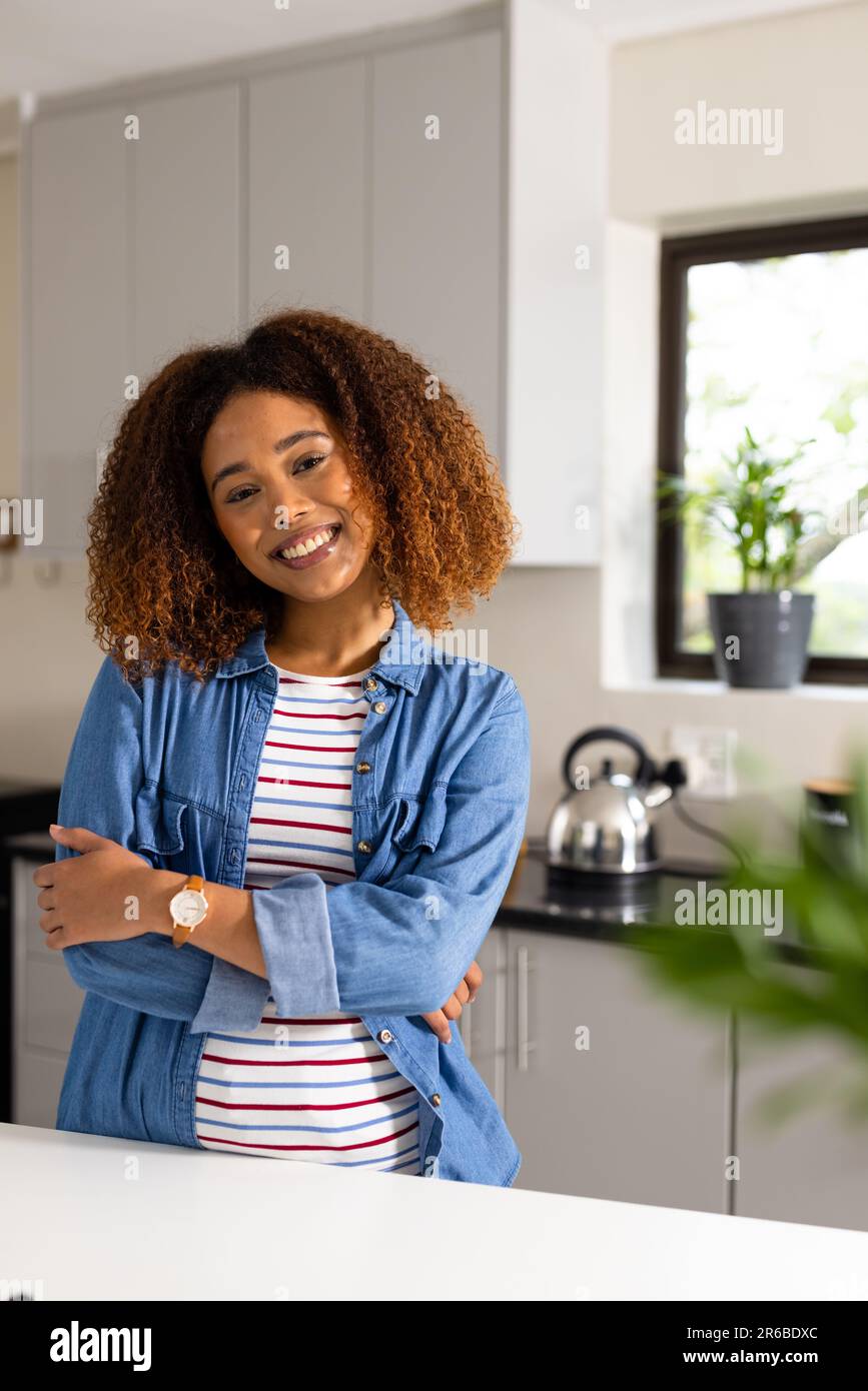 Portrait of happy biracial woman with curly hair smiling in kitchen, with copy space Stock Photo