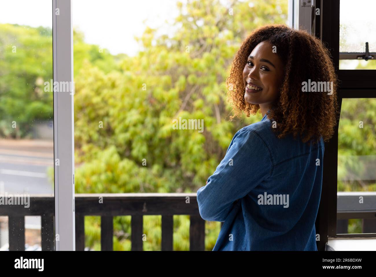Portrait of happy biracial woman with curly hair on balcony, turning and smiling, with copy space Stock Photo