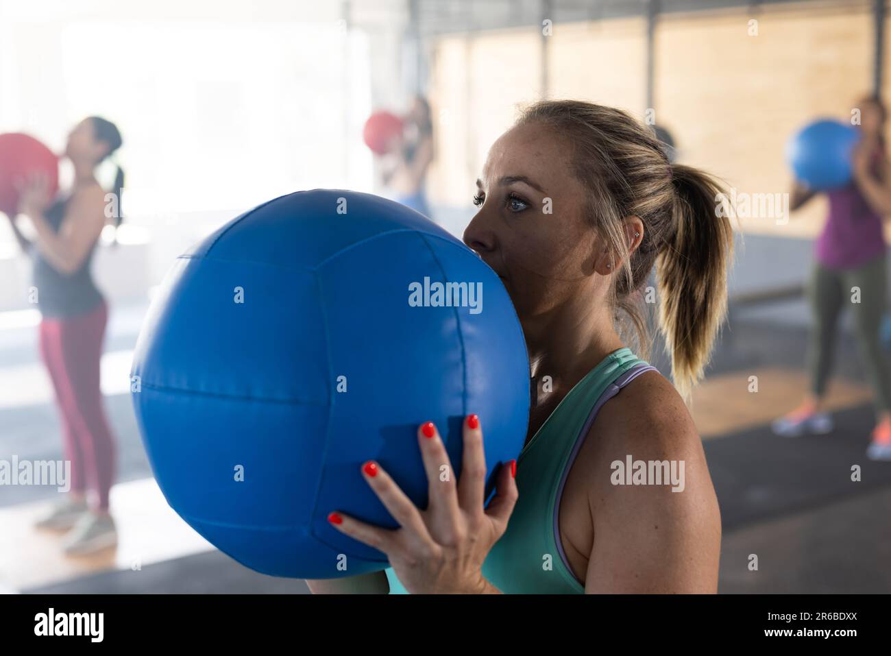 Confident caucasian young woman exercising with blue fitness ball in heath club, copy space Stock Photo