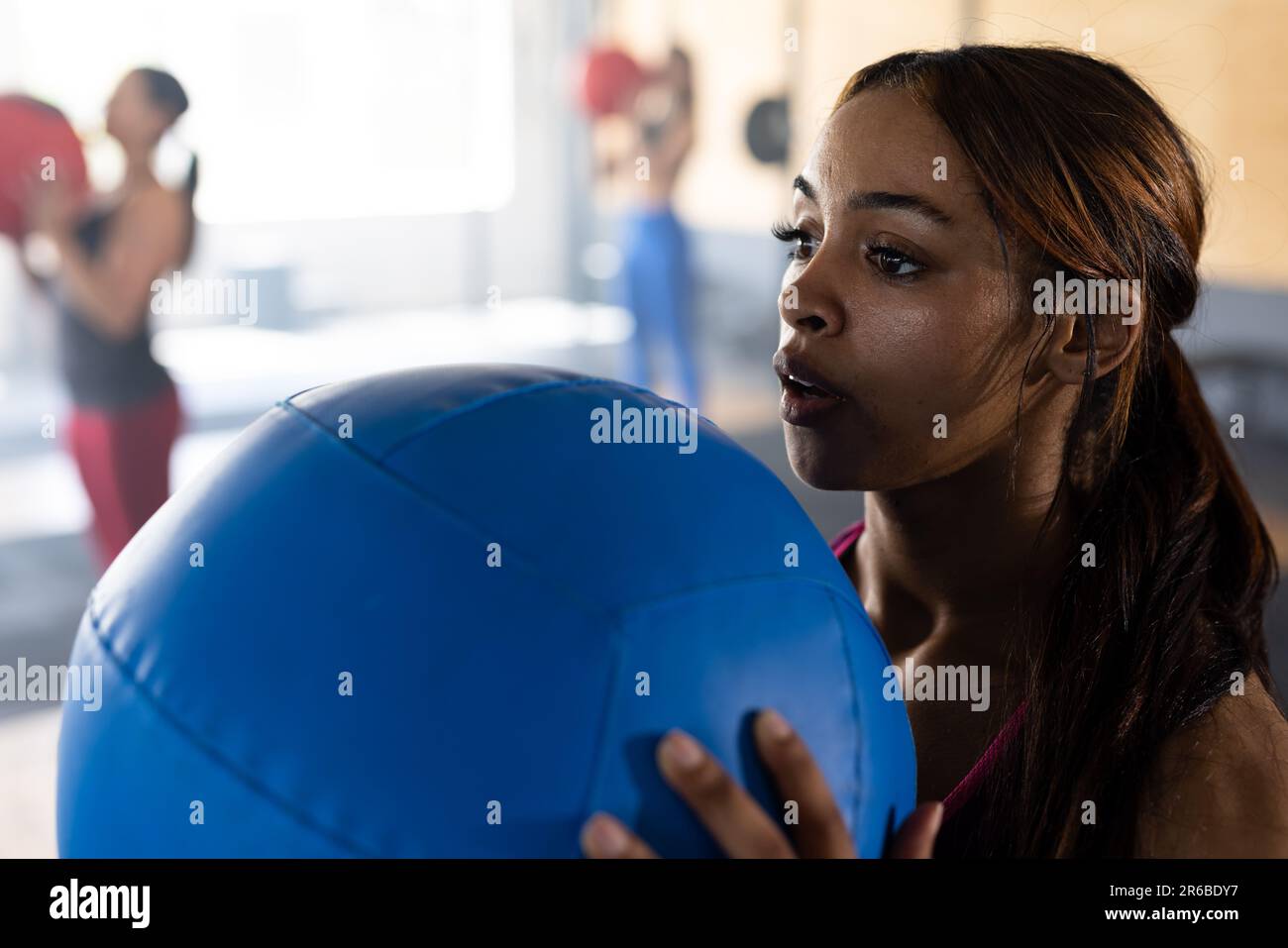 Confident biracial young woman exercising with blue fitness ball in heath club, copy space Stock Photo