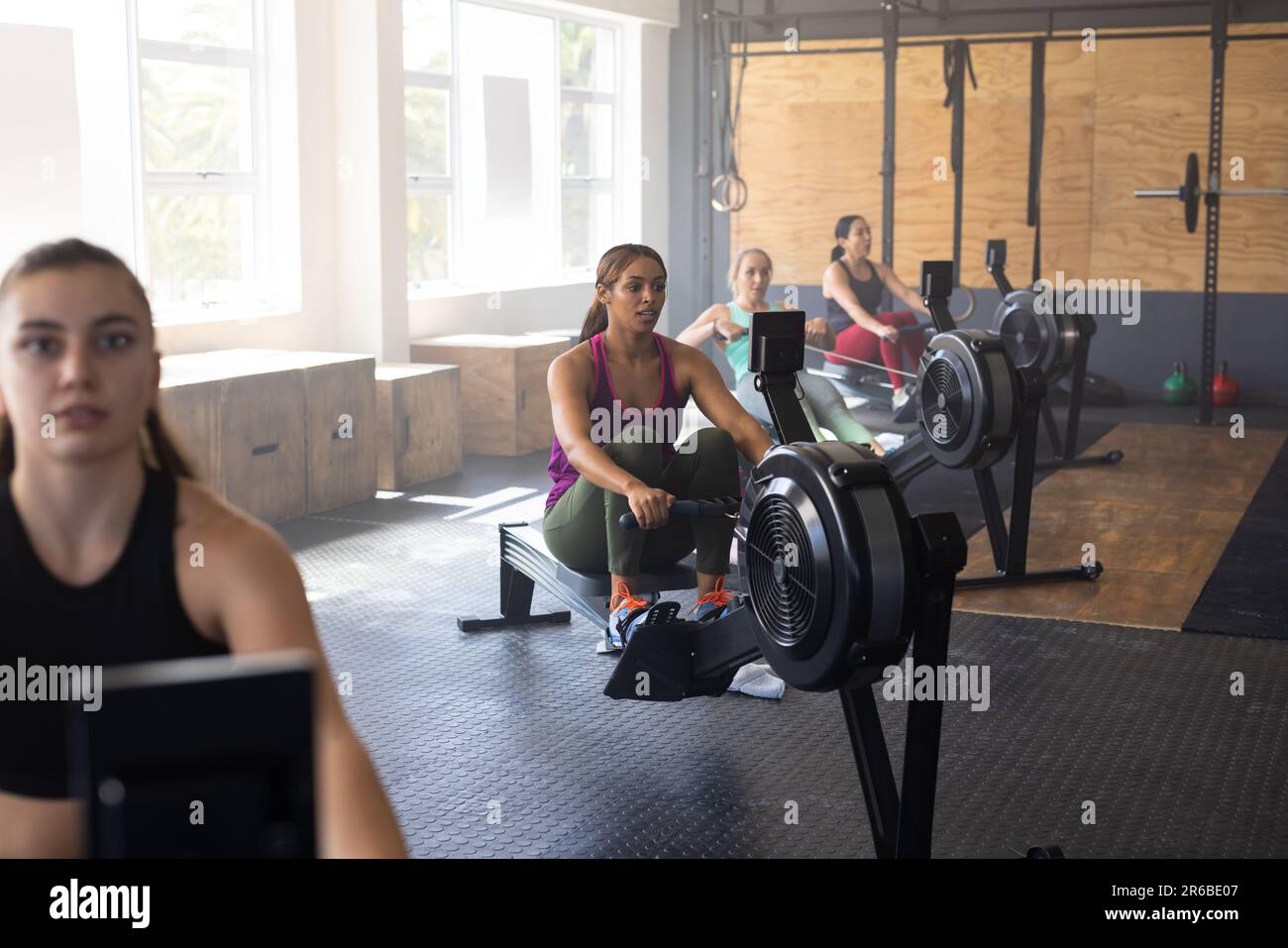 Multiracial female friends exercising with dedication on rowing machines in health club, copy space Stock Photo