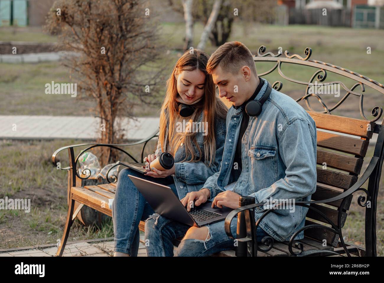 man and a woman with a laptop and tablet while working using laptop, sitting on the bench in park Stock Photo