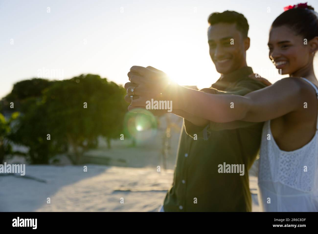 Smiling newlywed caucasian couple holding hands and dancing against clear sky at beach, copy space Stock Photo