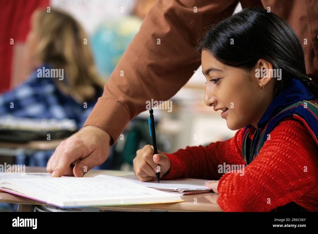 Teacher helping and observing a female asian american studennt who is working at heer desk Stock Photo