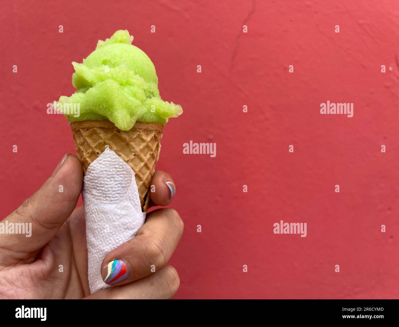 Hand with nail art manicure swirl design holding a ice cream cone with a scoop of lime green sorbet Stock Photo