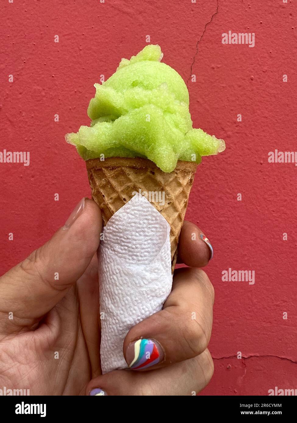 Hand with nail art manicure swirl design holding a ice cream cone with a scoop of lime green sorbet Stock Photo