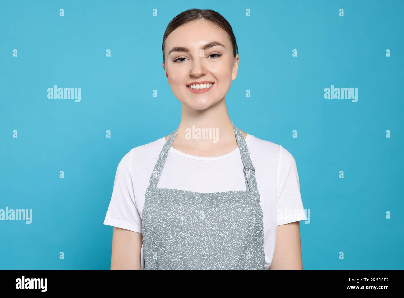 Beautiful young woman in clean apron with pattern on light blue ...