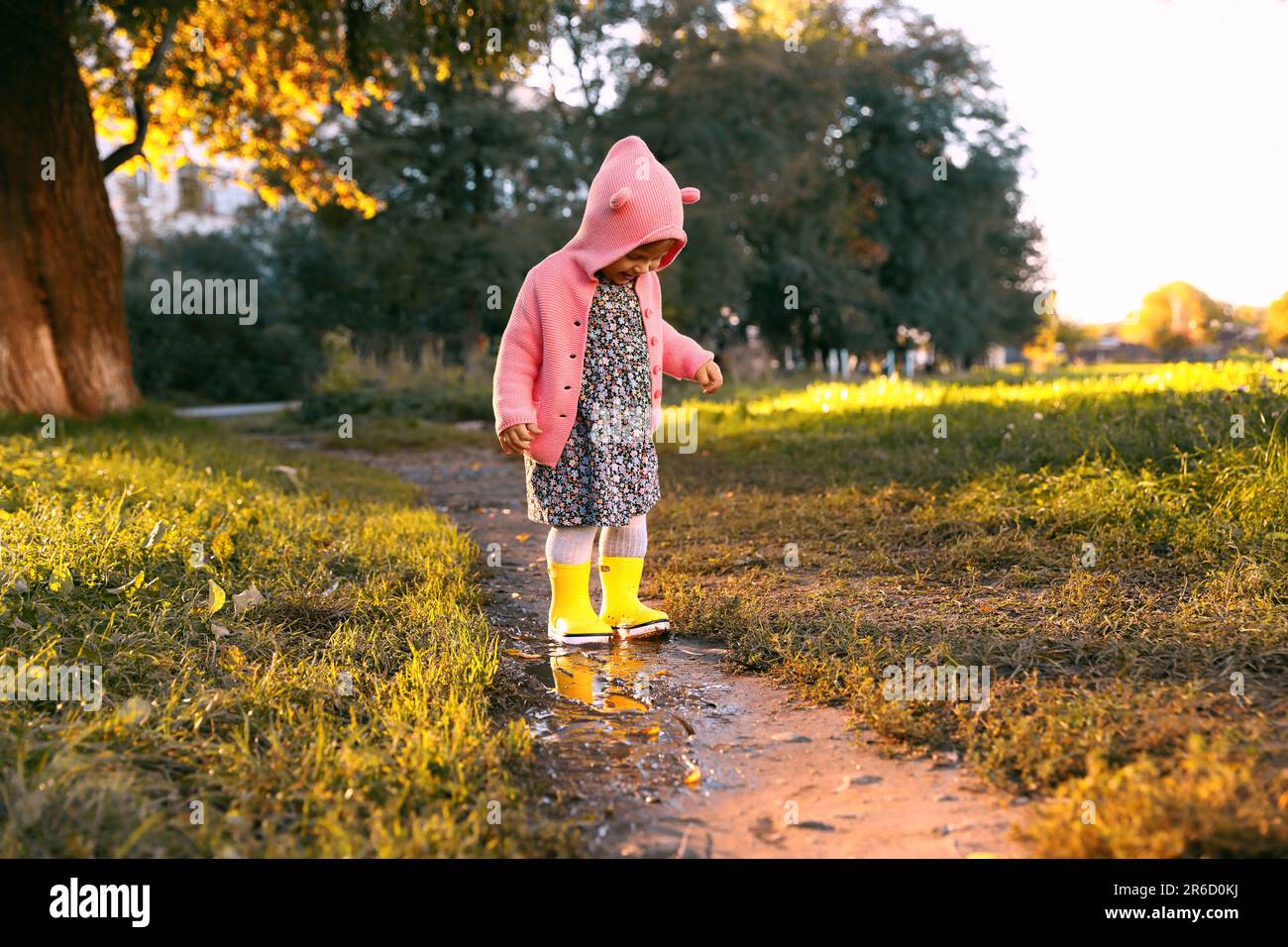 Little girl wearing rubber boots standing in puddle outdoors. Autumn ...