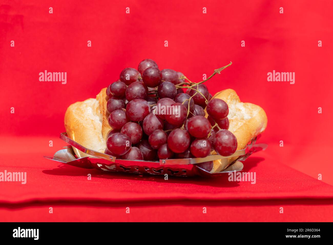 Wine glass, bread and grapes on red cloth in hard light. Symbolism of