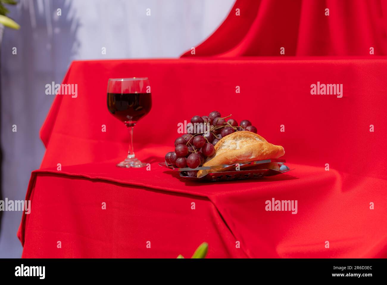 Wine glass, bread and grapes on red cloth in hard light. Symbolism of