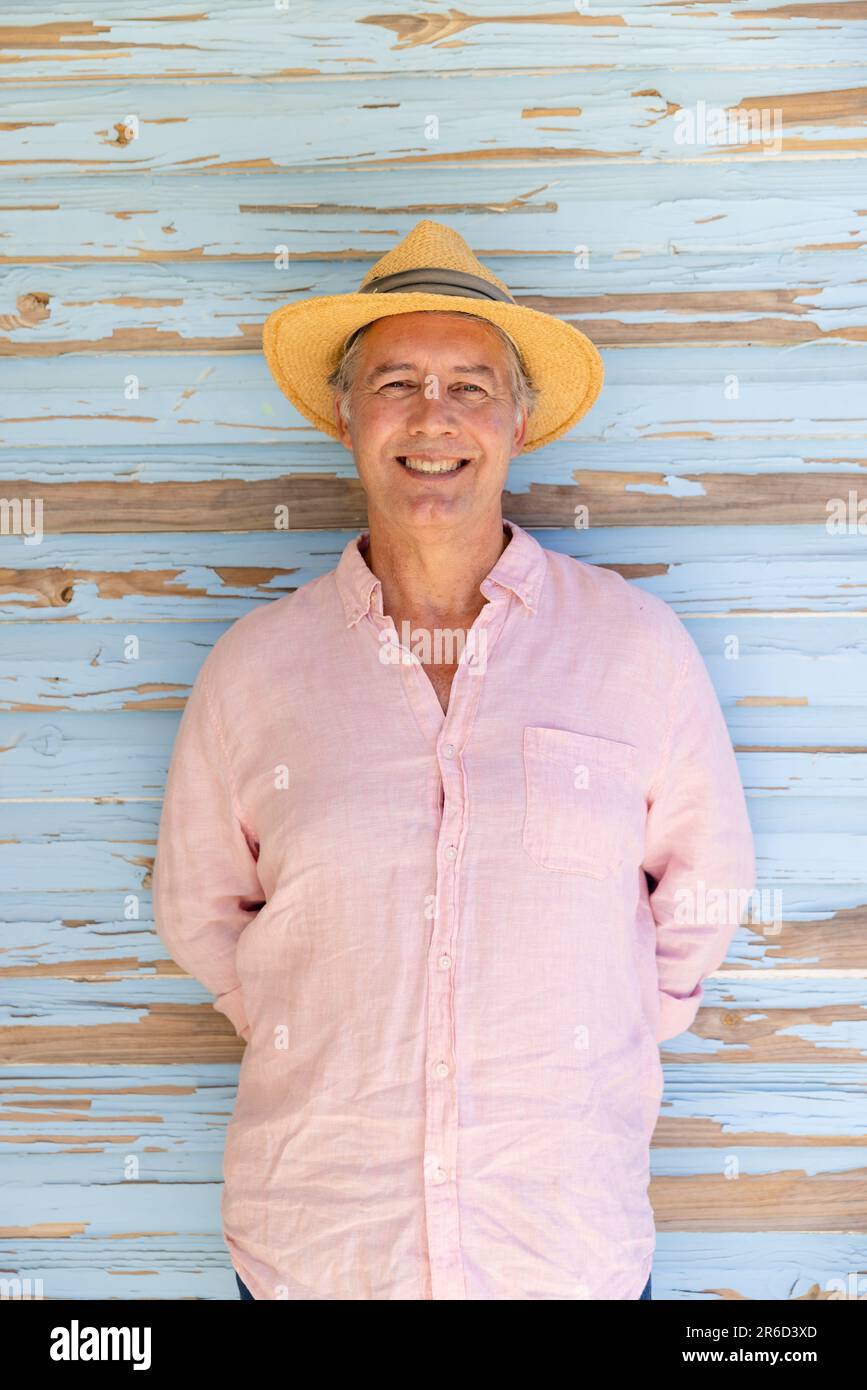Portrait of smiling caucasian senior man wearing hat and standing against wooden wall, copy space Stock Photo