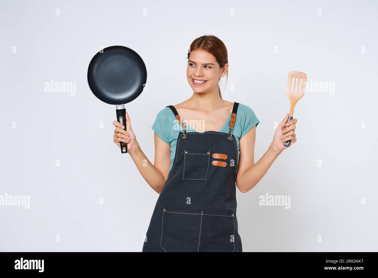 Young woman wearing kitchen apron cooking and holding pan and spatula isolated on white background. Stock Photo