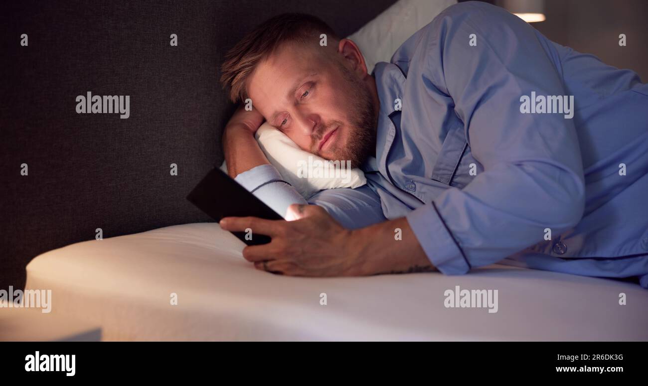 Man Lying On Bed Using Mobile Phone At Night Stock Photo
