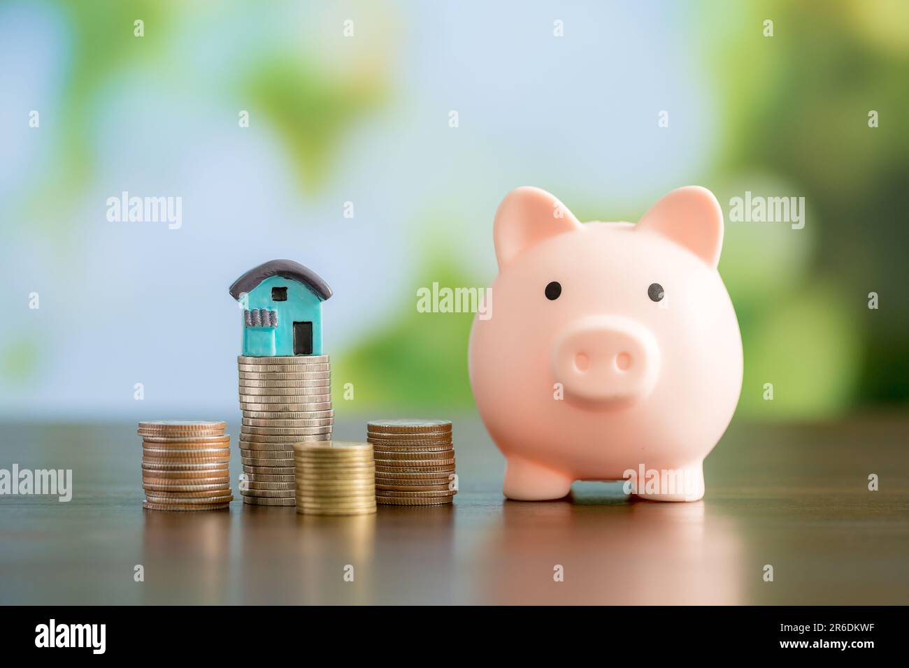 Mini house with piggy bank and coins money on natural green background ...