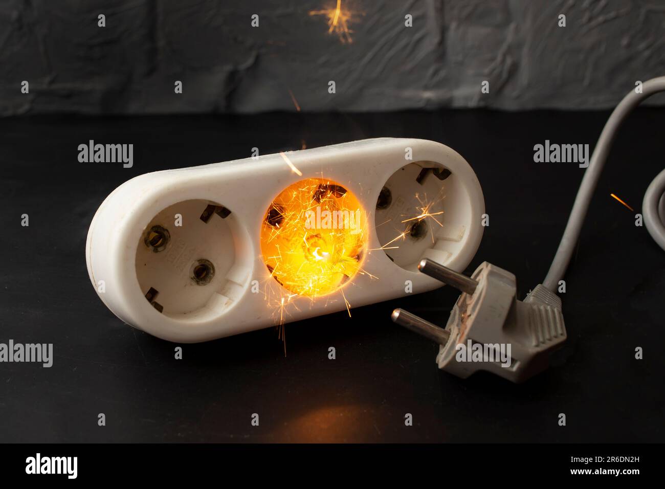 Short circuit sparks and flame in a outlet with an electrical cord on dark background Stock Photo