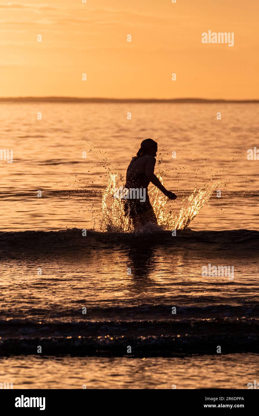 Silhouette of female swimmer having a splash in the Atlantic ocean in Ireland. Stock Photo