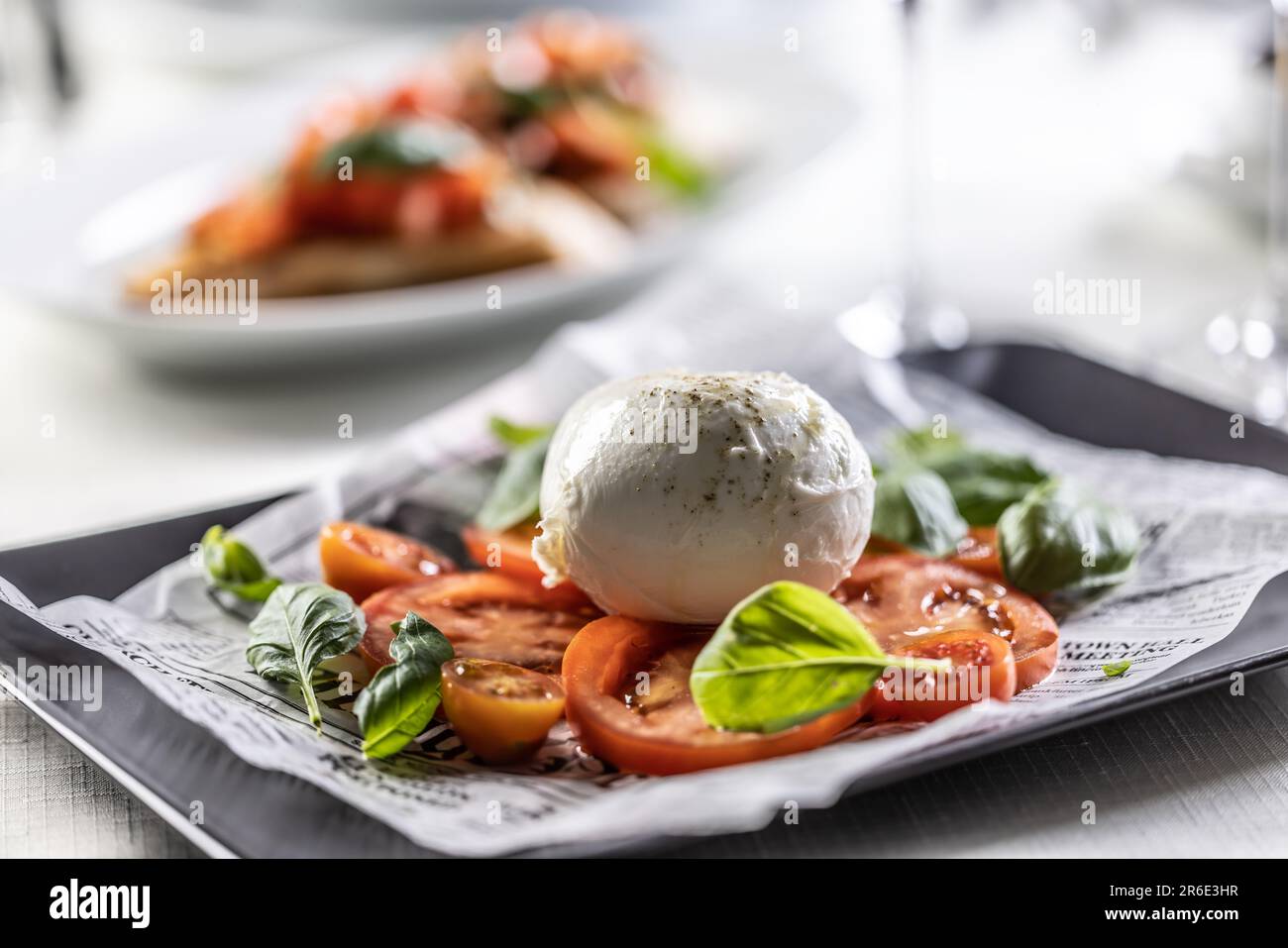 Caprese style salad with sliced tomatoes, basil and ball of buffalo mozzarella. Stock Photo