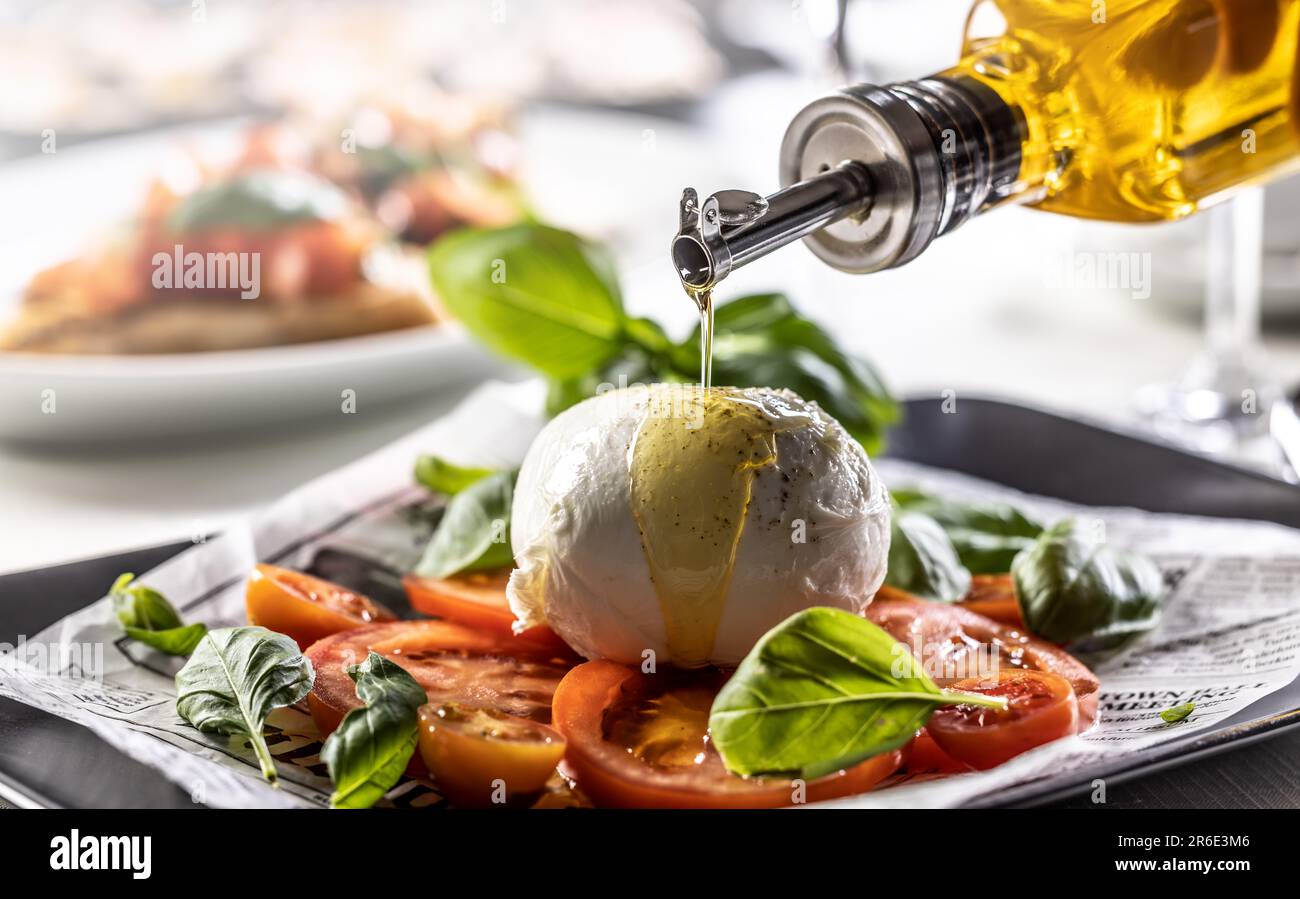 Olive oil poured over buffalo mozzarella ball on a differently styled Caprese salad. Stock Photo