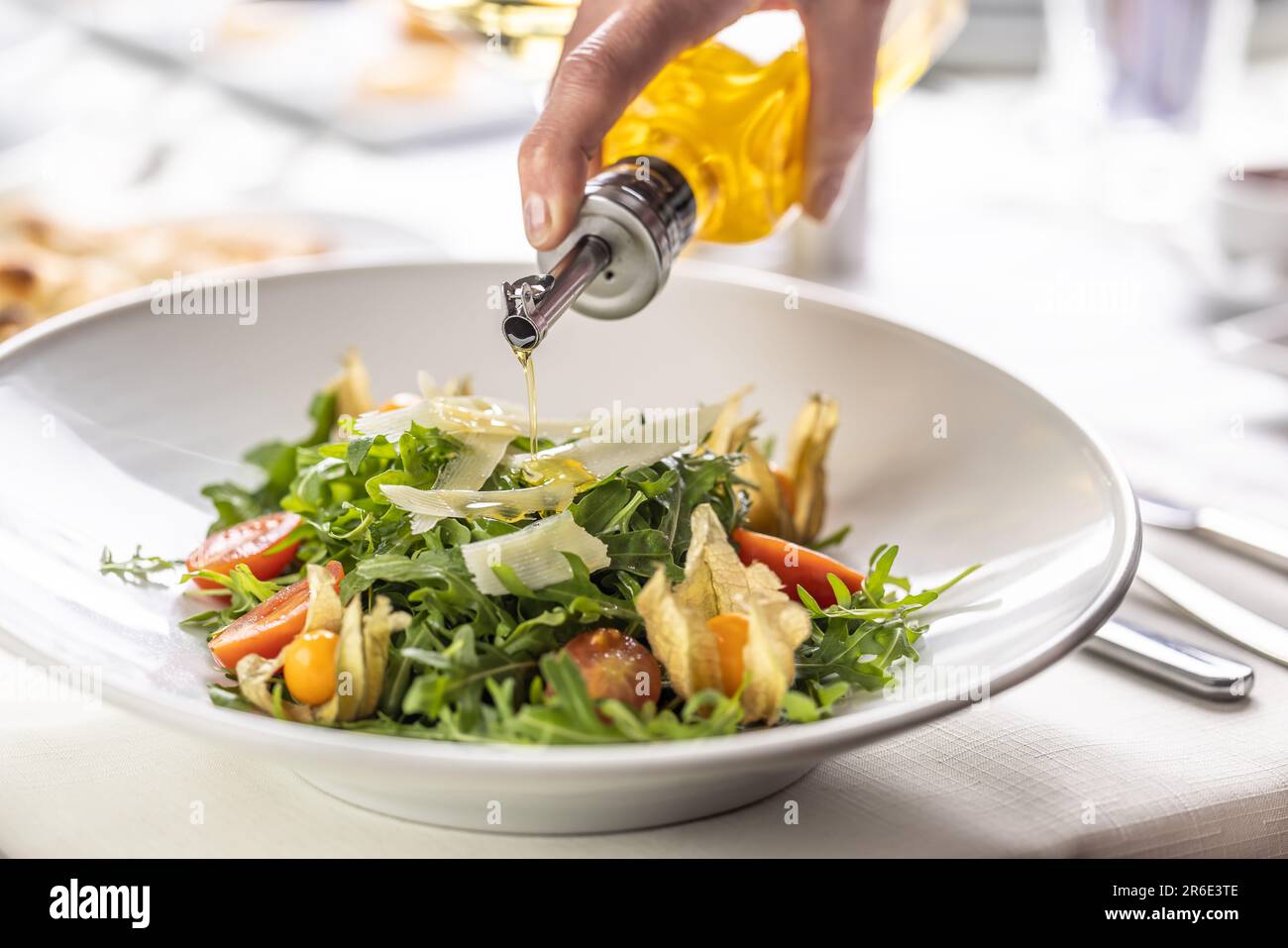 Olive oil pouring over a fresh rocket salad with parmesan shavings and physalis. Stock Photo