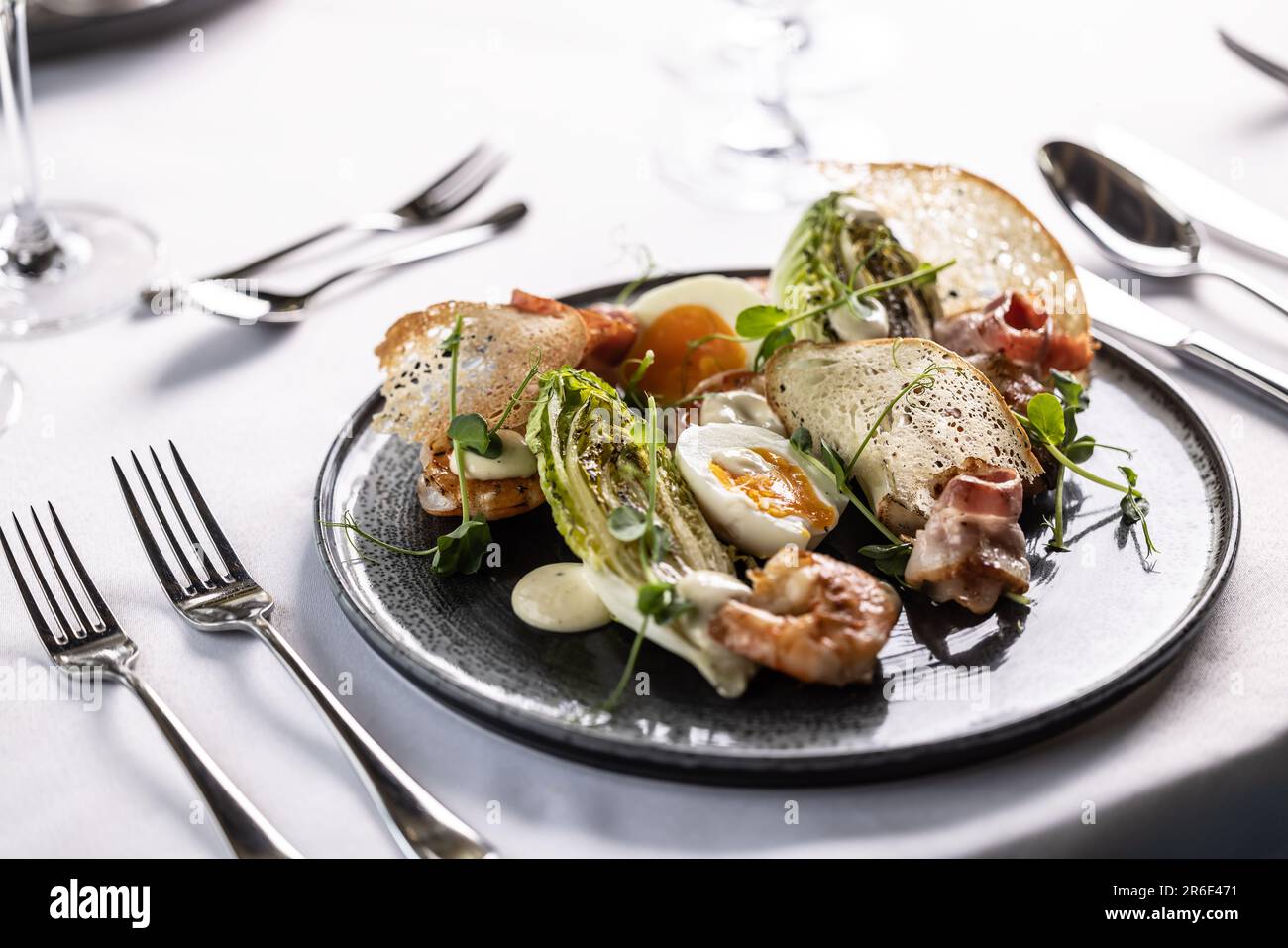 A twist of an elegant ceasar salad with shrimps served on a dark plate in a restaurant. Stock Photo