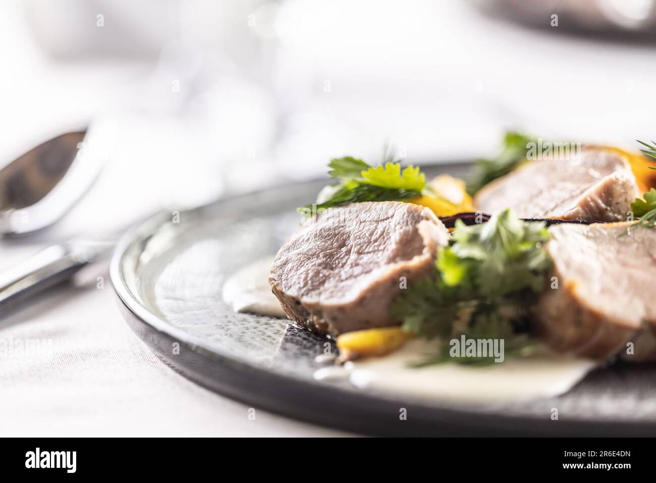 Detail of pork medallions with vegetables and dressing on a shallow dark plate. Stock Photo