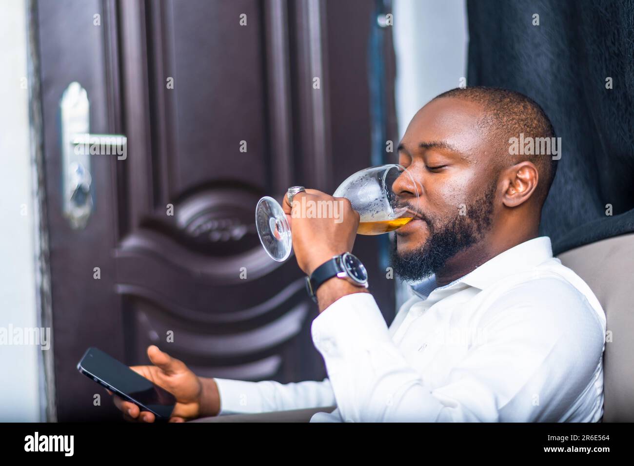 young adult african businessman with beards having refreshment from wineglass while using mobile phone. Technology Stock Photo