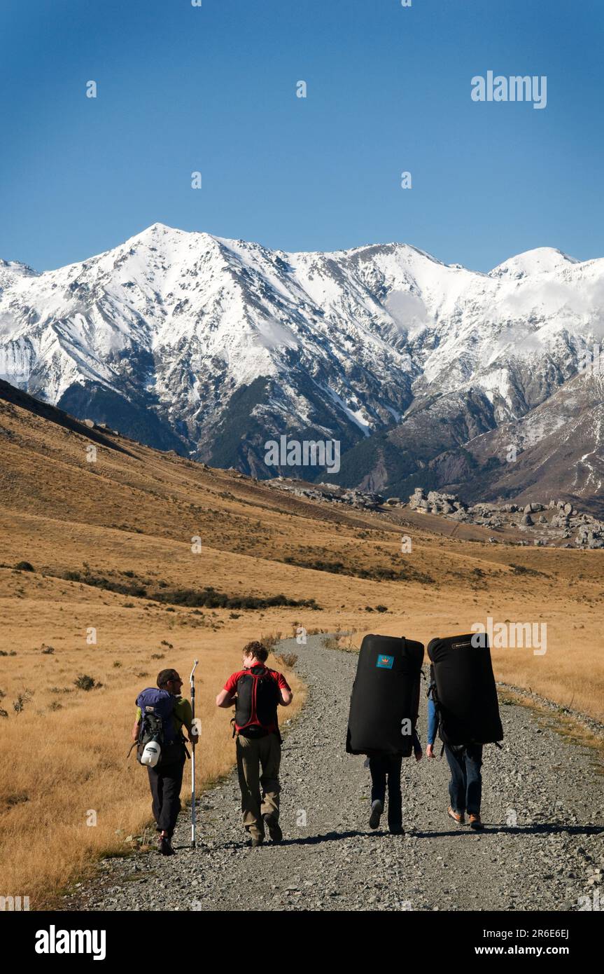 Rock climbers walk a farm road out to limestone boulders in the Castle Hill Basin, New Zealand. Stock Photo