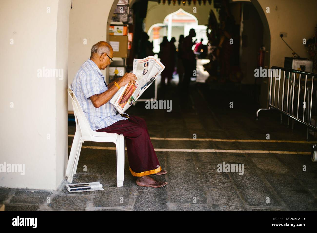 Man reads newspaper outside Hindu temple in Southeast Asia Stock Photo