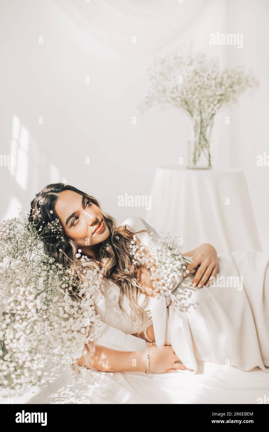 creative portrait of female laying by white flowers on white backdrop Stock Photo
