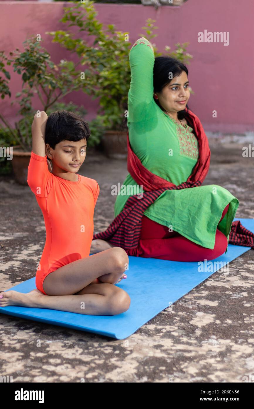 An Indian girl child and mother practicing Gomukhasana yoga on yoga mat ...