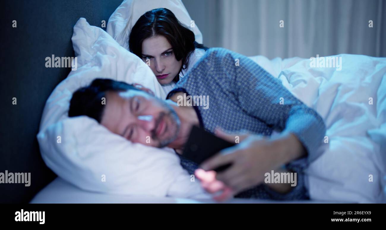 Woman Looking At Man Talking On Mobile Phone In Bedroom Stock Photo