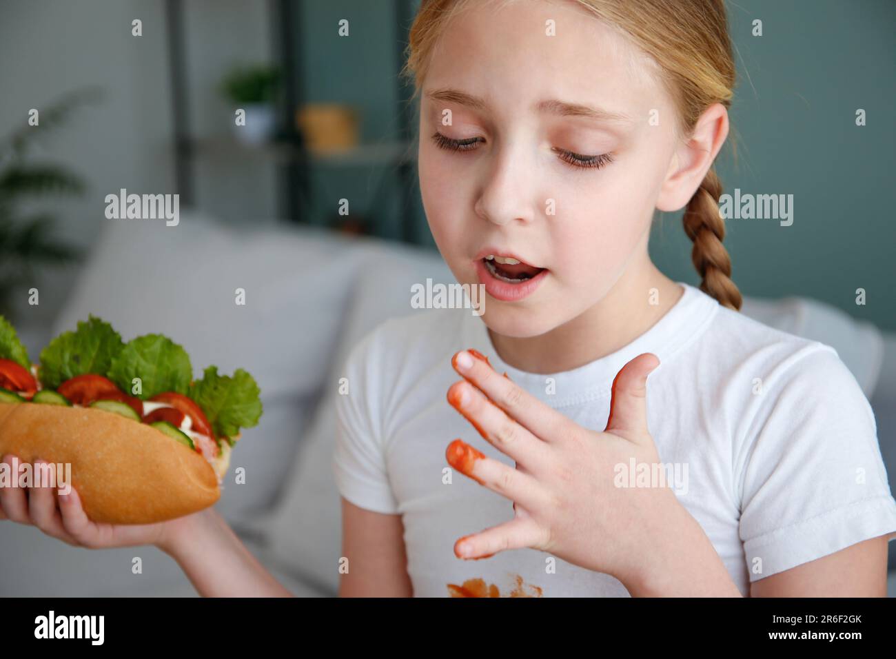 The child stained his clothes with ketchup. A girl eats a hot dog Stock