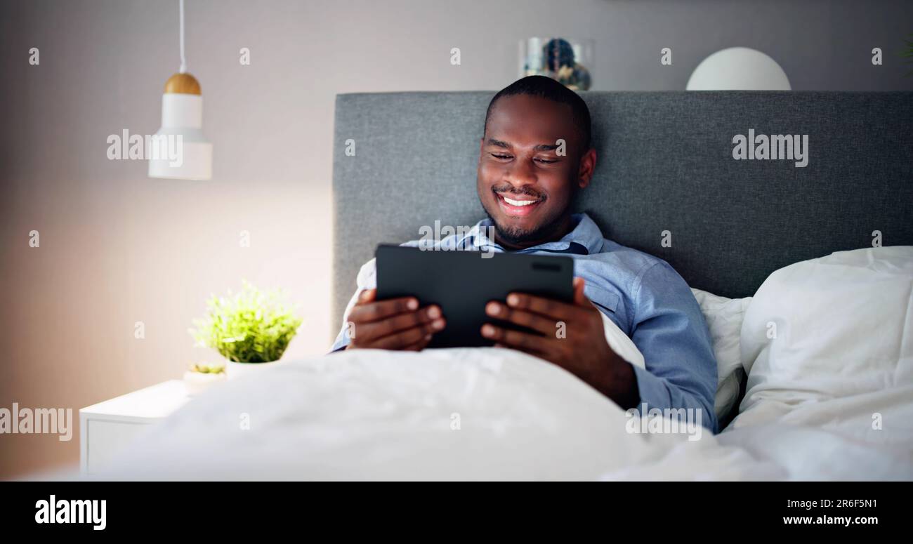 Man Lying On Bed Looking At Illuminated Digital Tablet Stock Photo