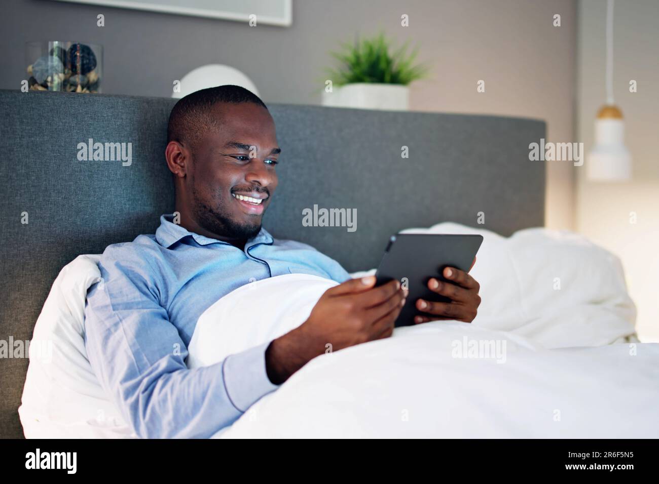 Man Lying On Bed Looking At Illuminated Digital Tablet Stock Photo
