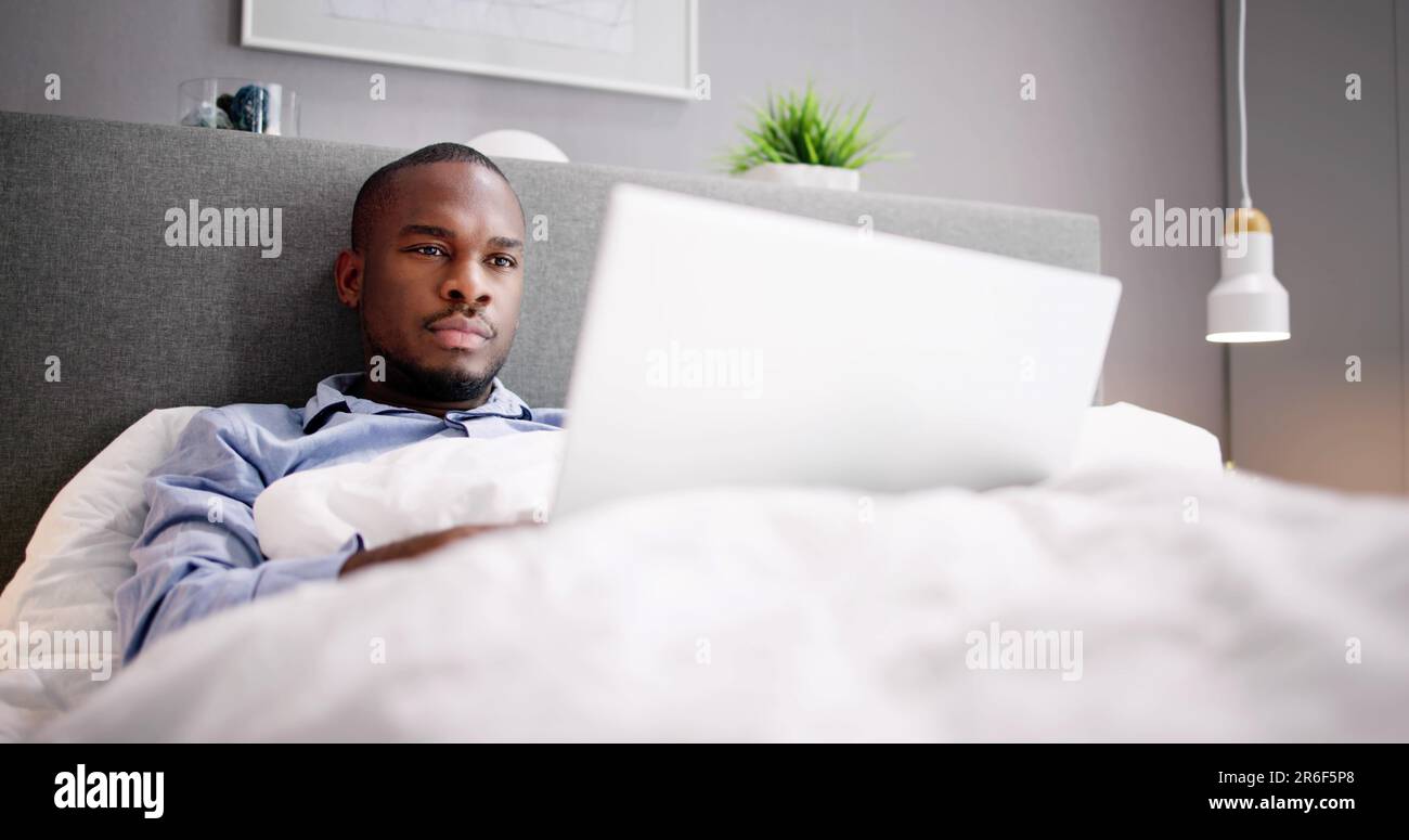Happy Man Sitting On Bed Using Laptop Stock Photo
