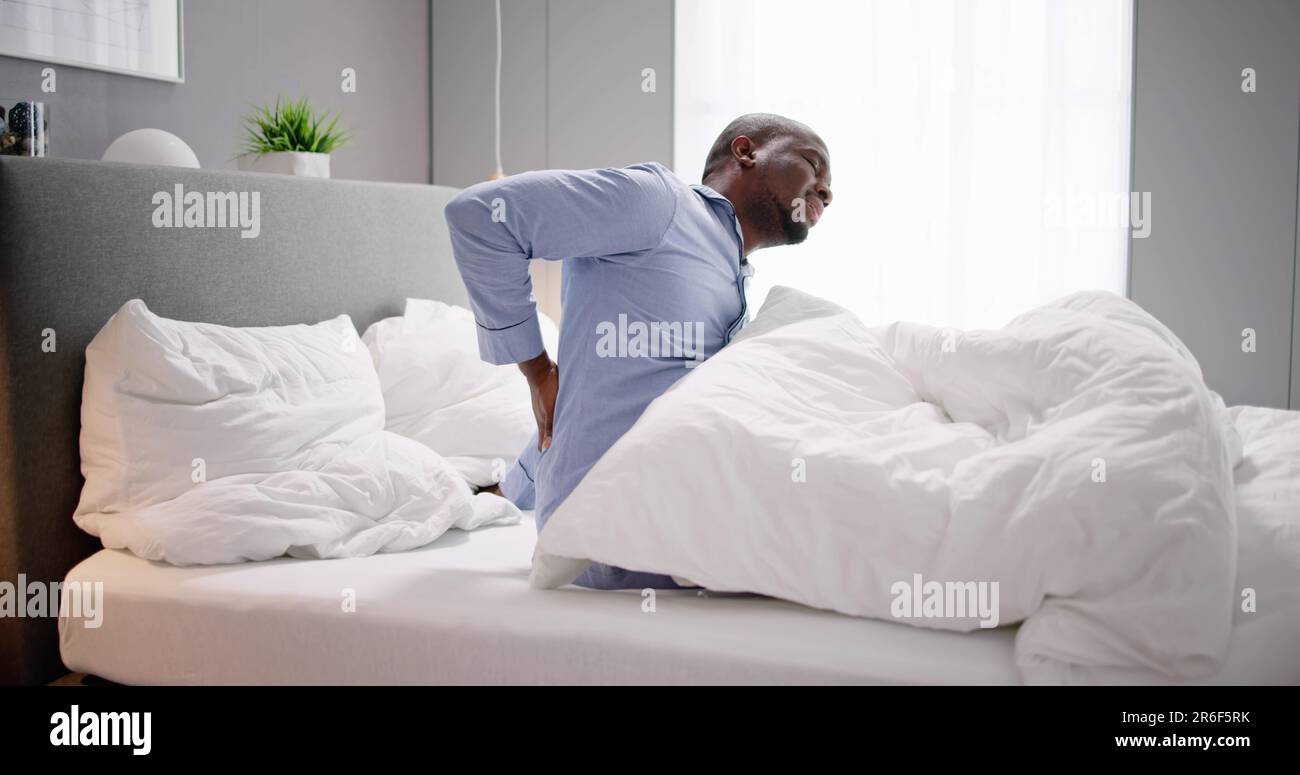 Man Sitting On Bed Suffering From Back Pain Stock Photo - Alamy