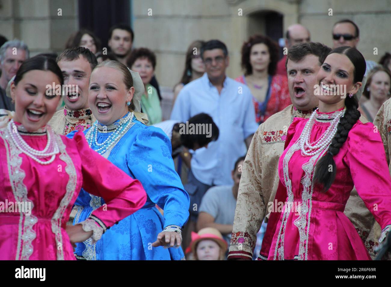 A group of cheerful young female performers standing on stage in front of a bustling audience, beaming with smiles and radiating joy Stock Photo