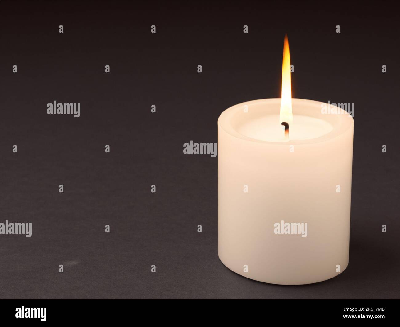 a lit candle on a black surface with a black background. . Stock Photo