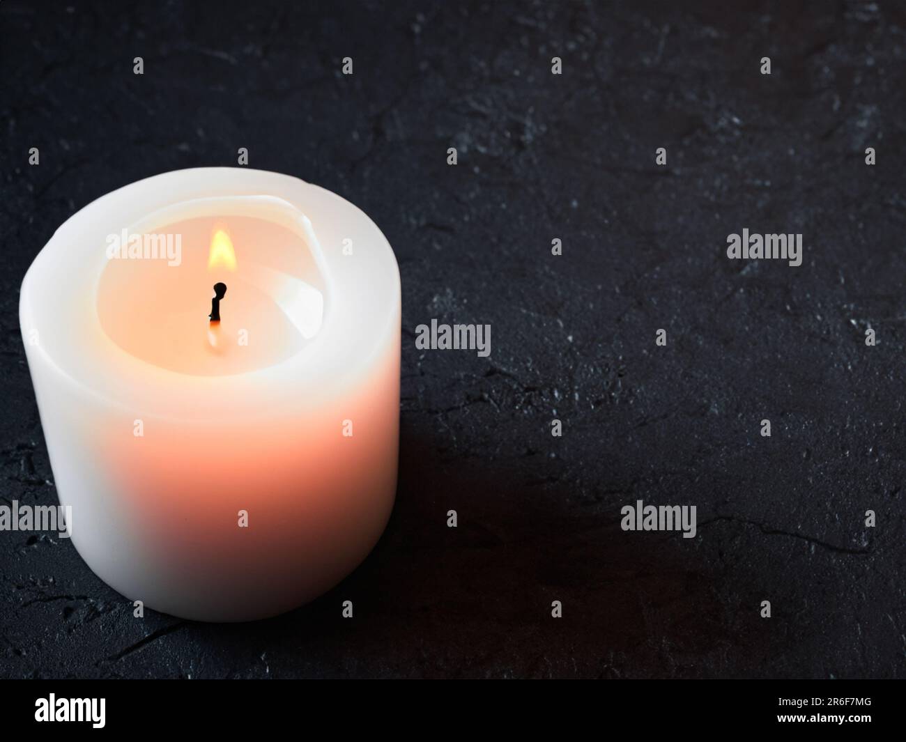 a lit candle on a black surface with a small candle in the middle. . Stock Photo