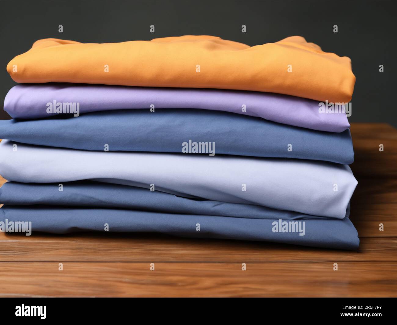 a stack of folded clothes on a wooden table with a black background. . Stock Photo