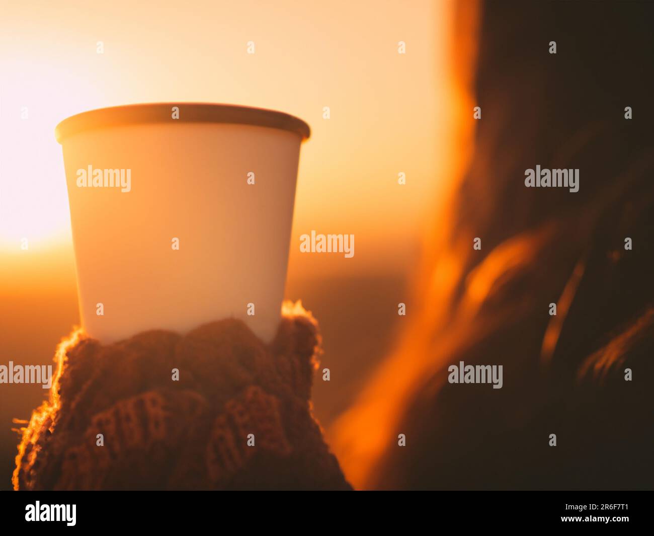 a woman holding a cup of coffee in her hand at sunset. . Stock Photo