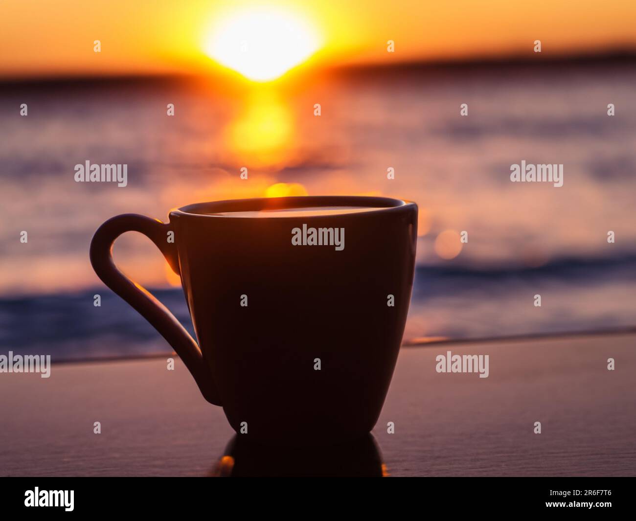 a coffee cup sitting on a table next to the ocean. . Stock Photo