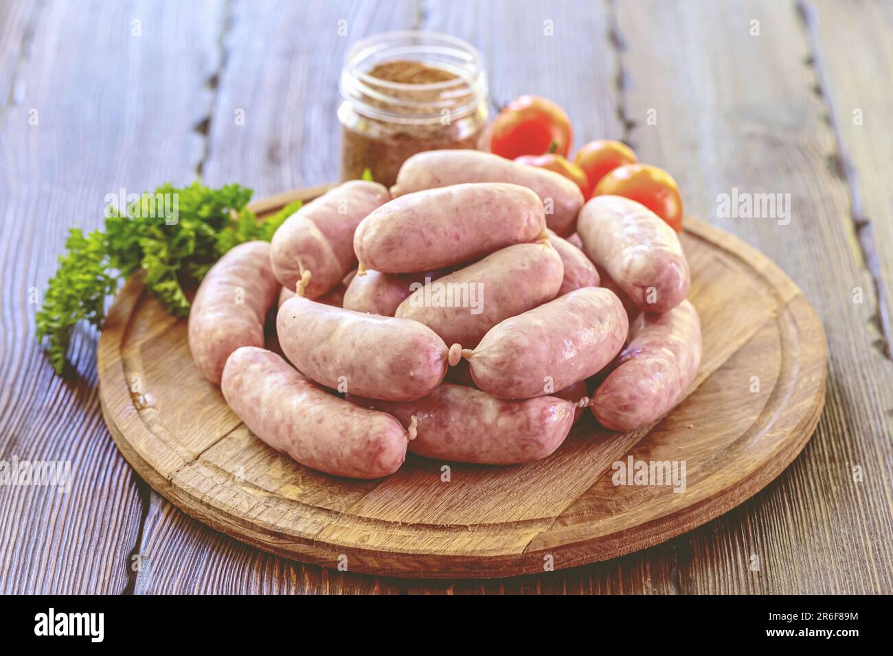 A wooden plate with an array of raw sausages and assorted vegetables on top of a wooden table surface Stock Photo